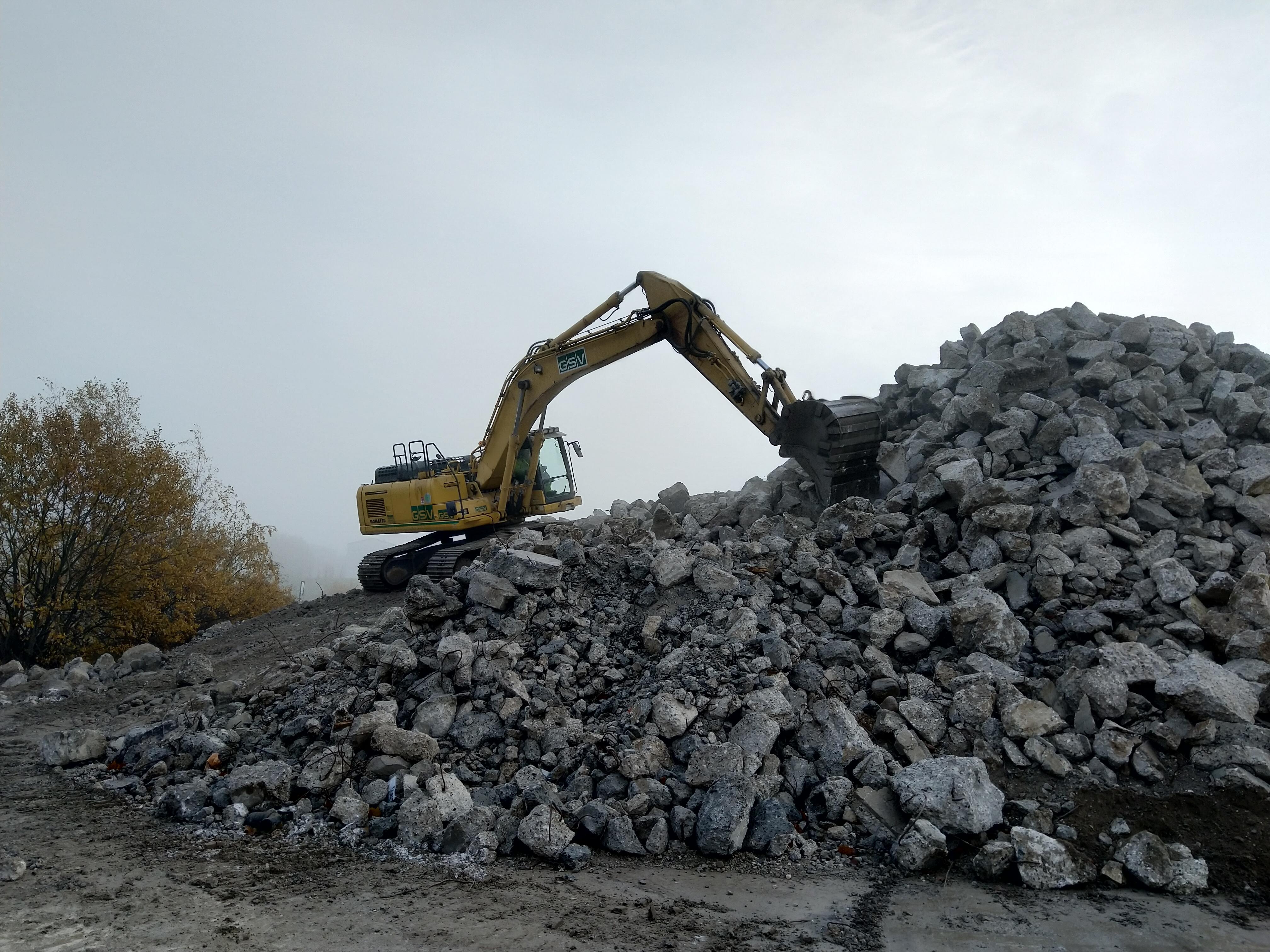 Et bjerg af nedknust beton med en gravemaskine på toppen.