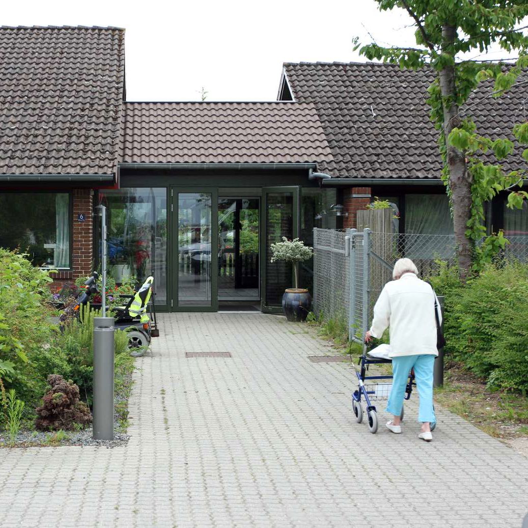 Plejecenter i Roskilde Kommune. En ældre borger med rollator er på vej mod indgangen.