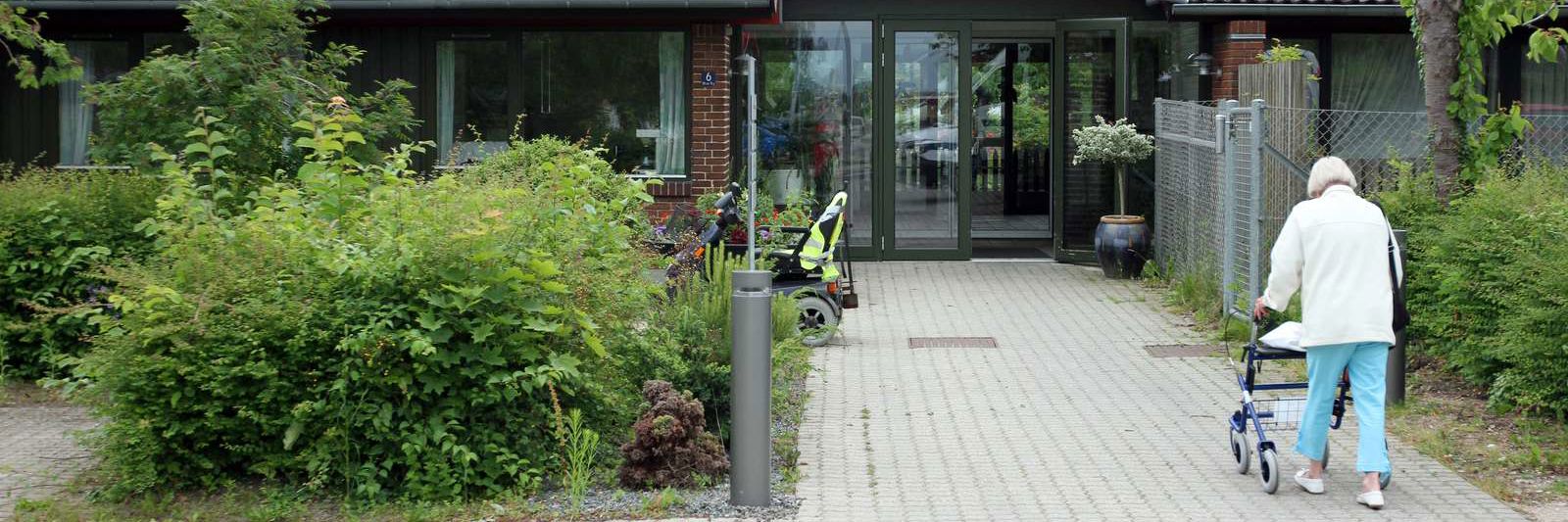 Plejecenter i Roskilde Kommune. En ældre borger med rollator er på vej mod indgangen.
