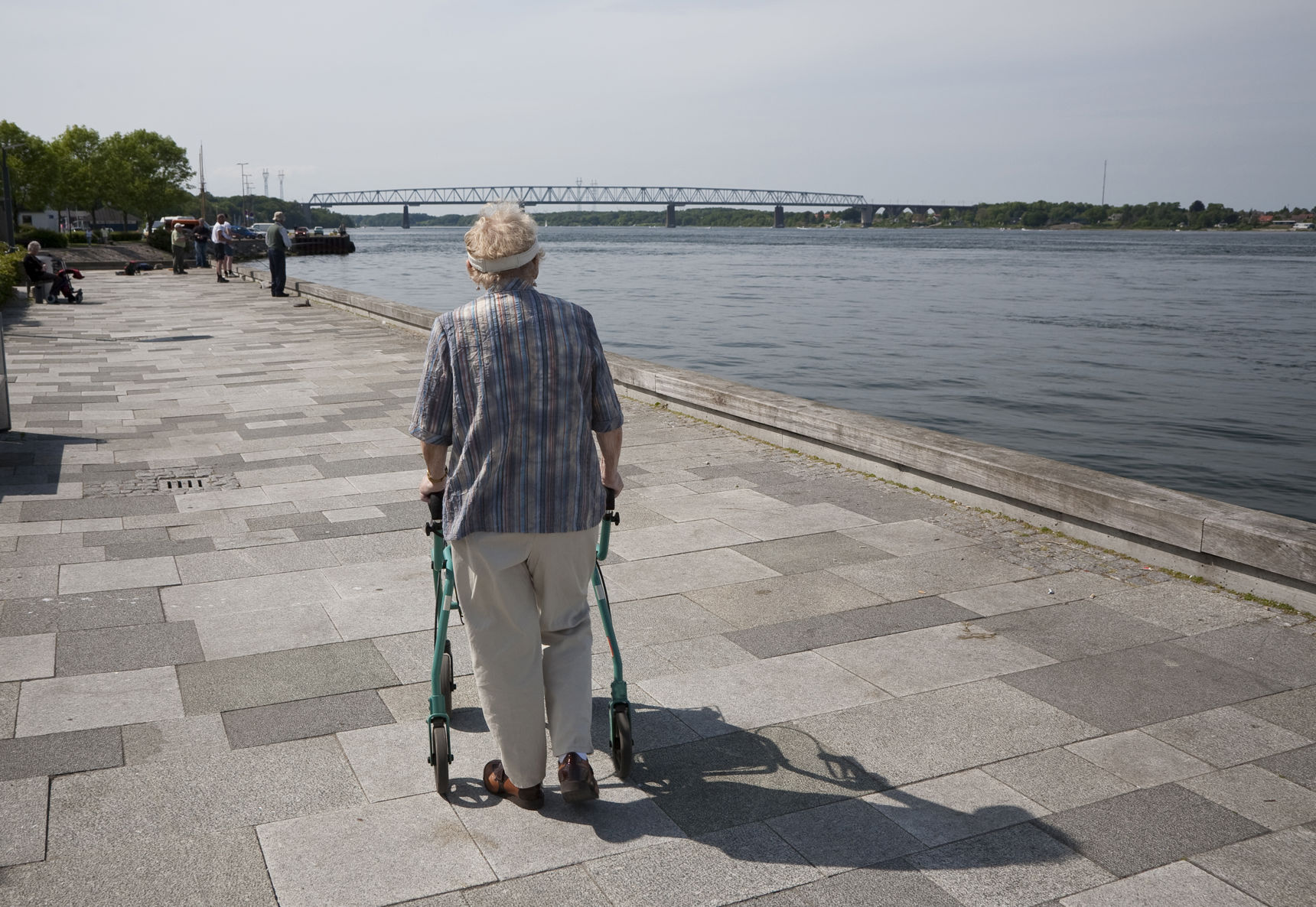 Ældre person går langs en flod. Personen støtter sig op ad sin rollator.