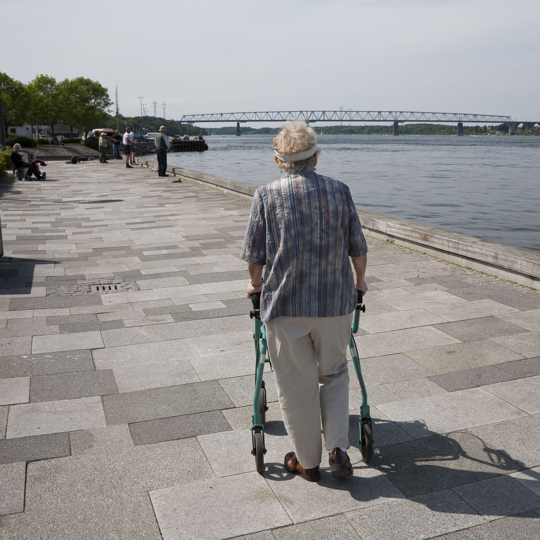 Ældre person går langs en flod. Personen støtter sig op ad sin rollator.