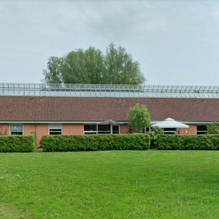 Ældrebolig Perlen. Der er en masse grønt græs. Bygningen er rød.