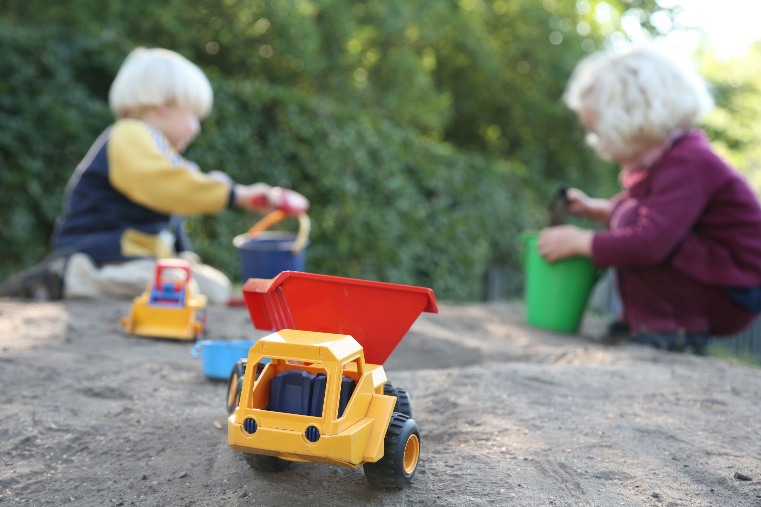 Børn, der leger i en sandkasse. Der er spande og skovle, og der er også små legetøjsbiler.