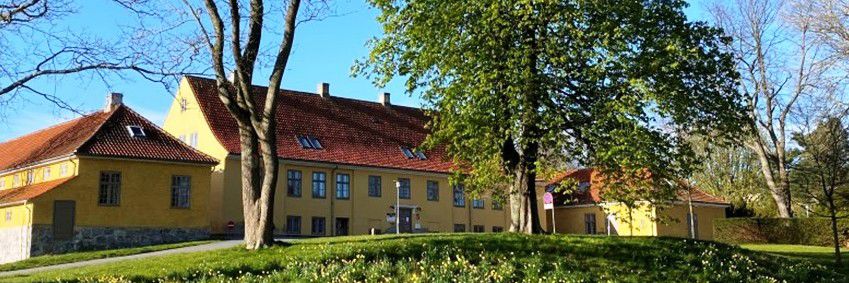 Gul bygning med rødt tag. Billedet er taget langt væk fra.