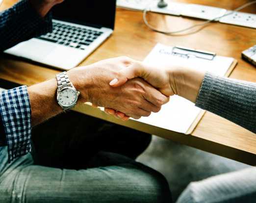 To personer giver hinanden hånden. Der ses en computer og en kontrakt i baggrunden.