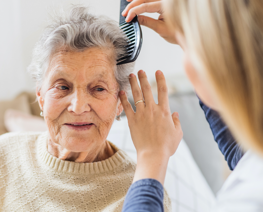Gammel dame får børstet sit hår af en lyshåret medarbejder. 