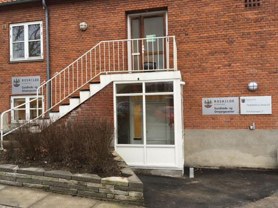 Indgang til Sundheds- og Omsorgscenter Nord. Bygningen er rød. Man skal op af en hvid trappe for at komme ind.