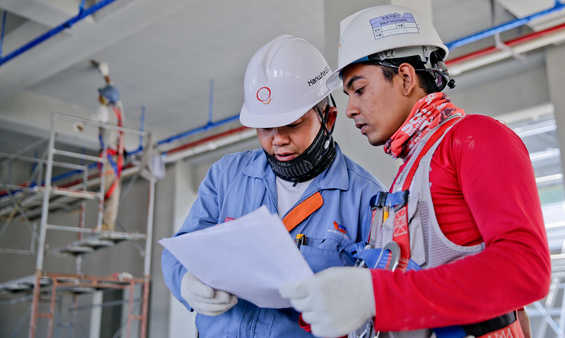 To personer kigger på et stykke papir. De er på en byggeplads.